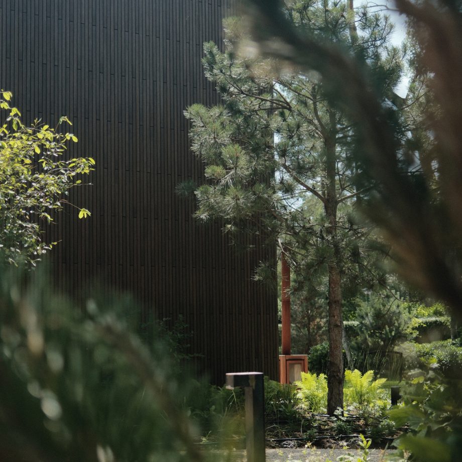 De bestaande omgeving vormde daarbij het uitgangspunt. Zelfs de karakteristieke dennenbomen zijn bewust toegevoegd om het gevoel te creëren dat het landschap al jarenlang onderdeel is van de plek. Duurzame materialen, zoals de bamboehouten gevelbekleding, sluiten naadloos aan op deze natuurlijke uitstraling en versterken de verbinding tussen woning en omgeving. Het resultaat is een buitenruimte die rust uitstraalt, opgaat in haar omgeving en de relatie tussen binnen en buiten op een vanzelfsprekende manier voelbaar maakt.